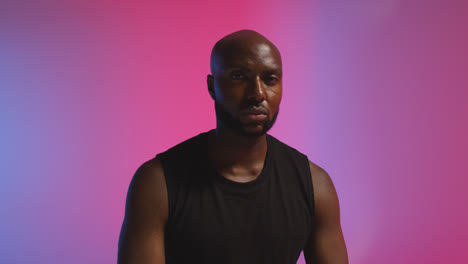 Studio-Portrait-Shot-Of-Male-Athlete-Wearing-Sports-Vest-Against-Pink-And-Blue-Lit-Background